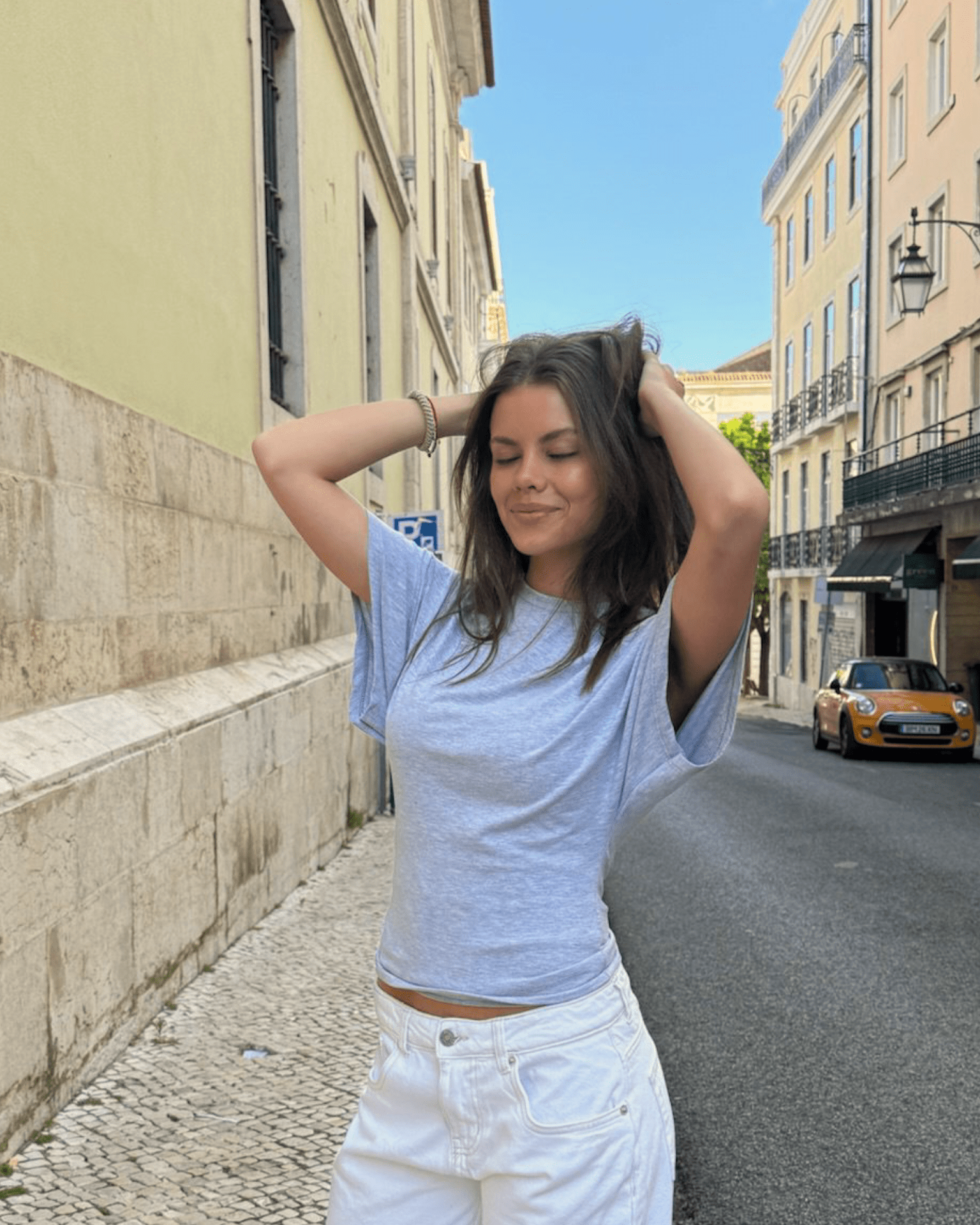 Lys grå Nina Angel top i blød jersey med løs pasform, stylet med hvide bukser på gaden