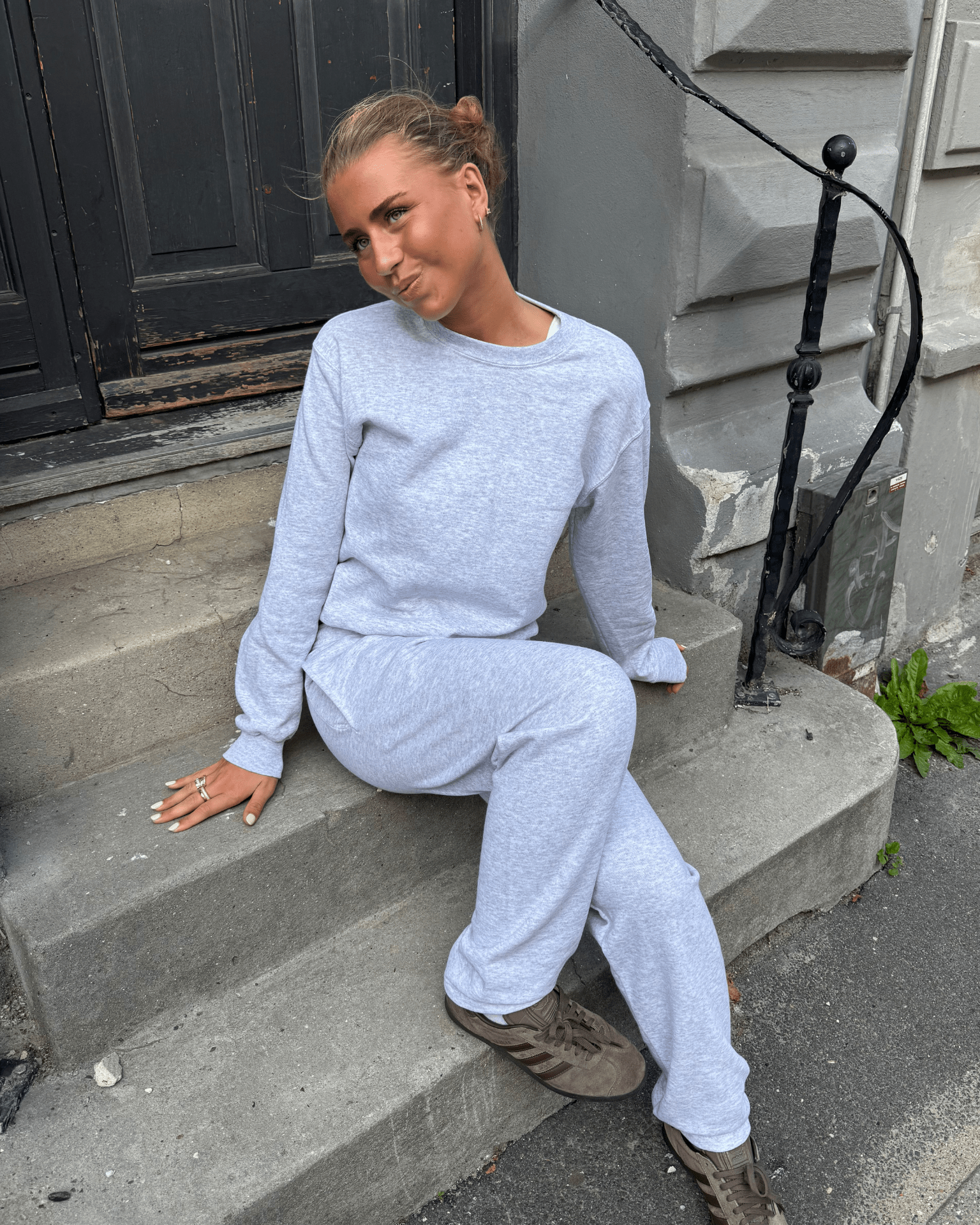Grå Fruit sweatshirt og matchende joggingbukser på model siddende på en trappe