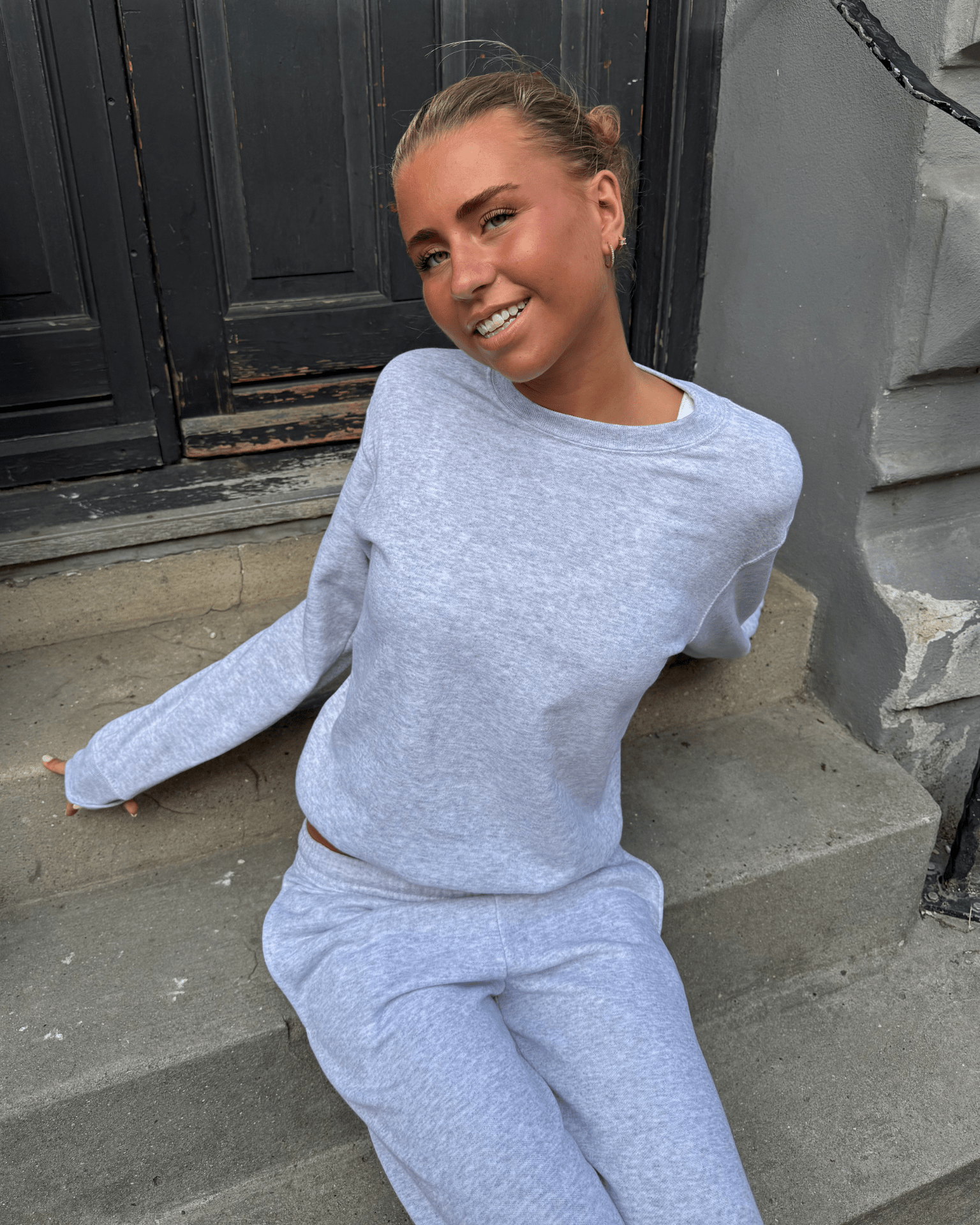 Grå klassisk sweatshirt og joggingbukser i bomuld på en model, der sidder på en trappe