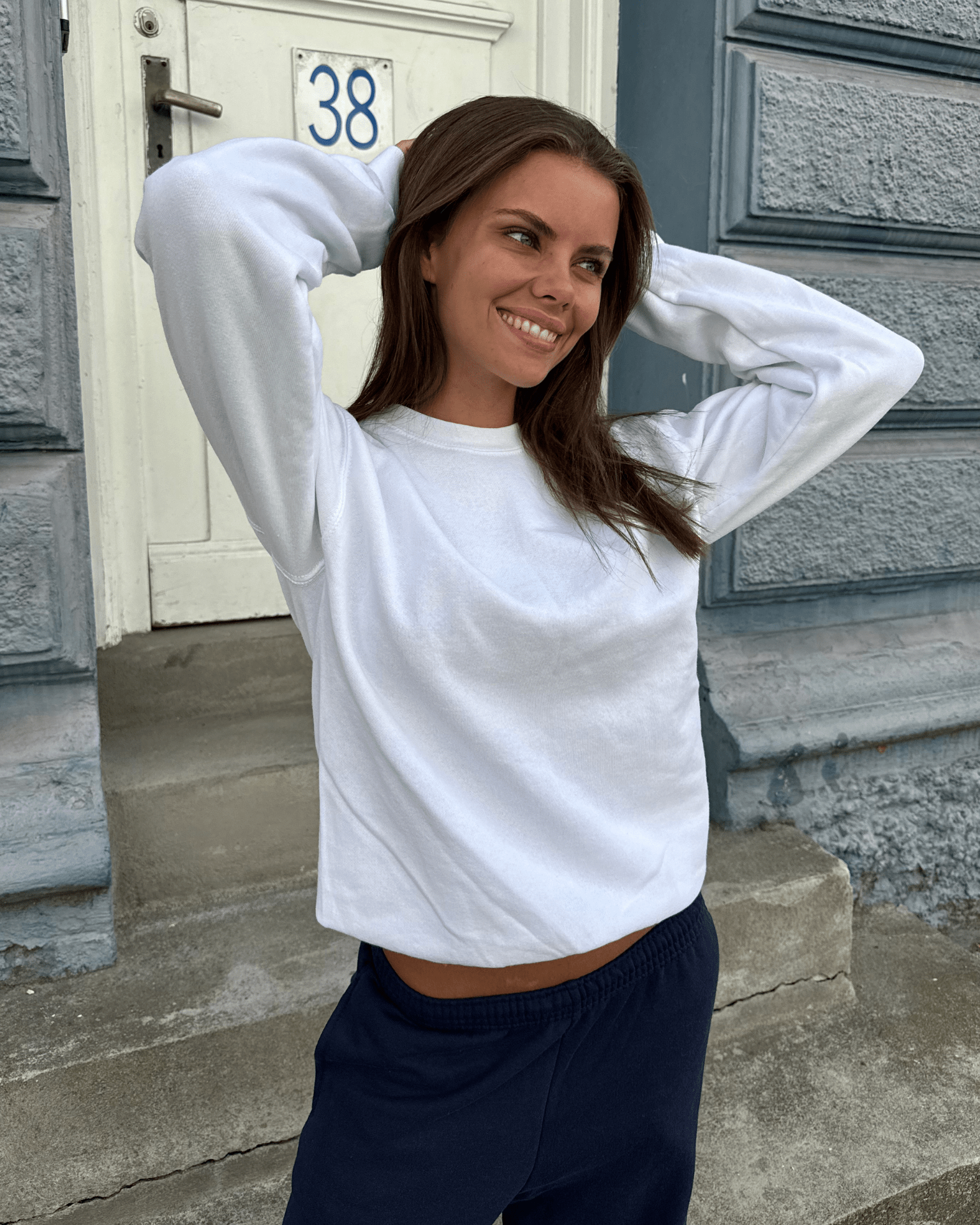 Smilende kvinde i hvid Fruit sweatshirt og mørke joggingbukser