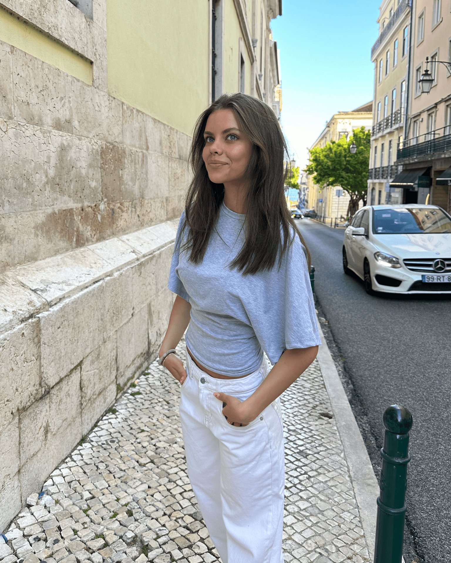 Lys grå Nina Angel top i blød jersey med løs pasform, stylet med hvide jeans på gaden.