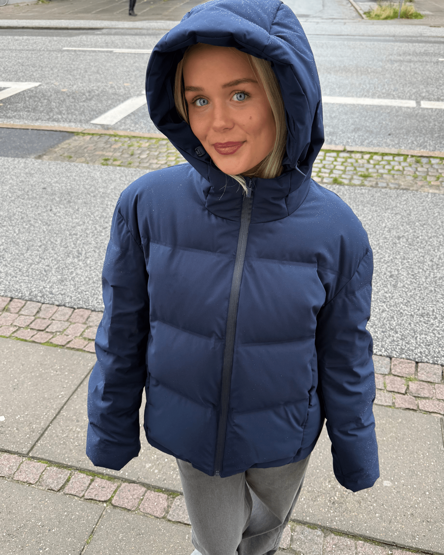 Navyblå Isa dunjakke med stor hætte båret af en kvinde på gaden