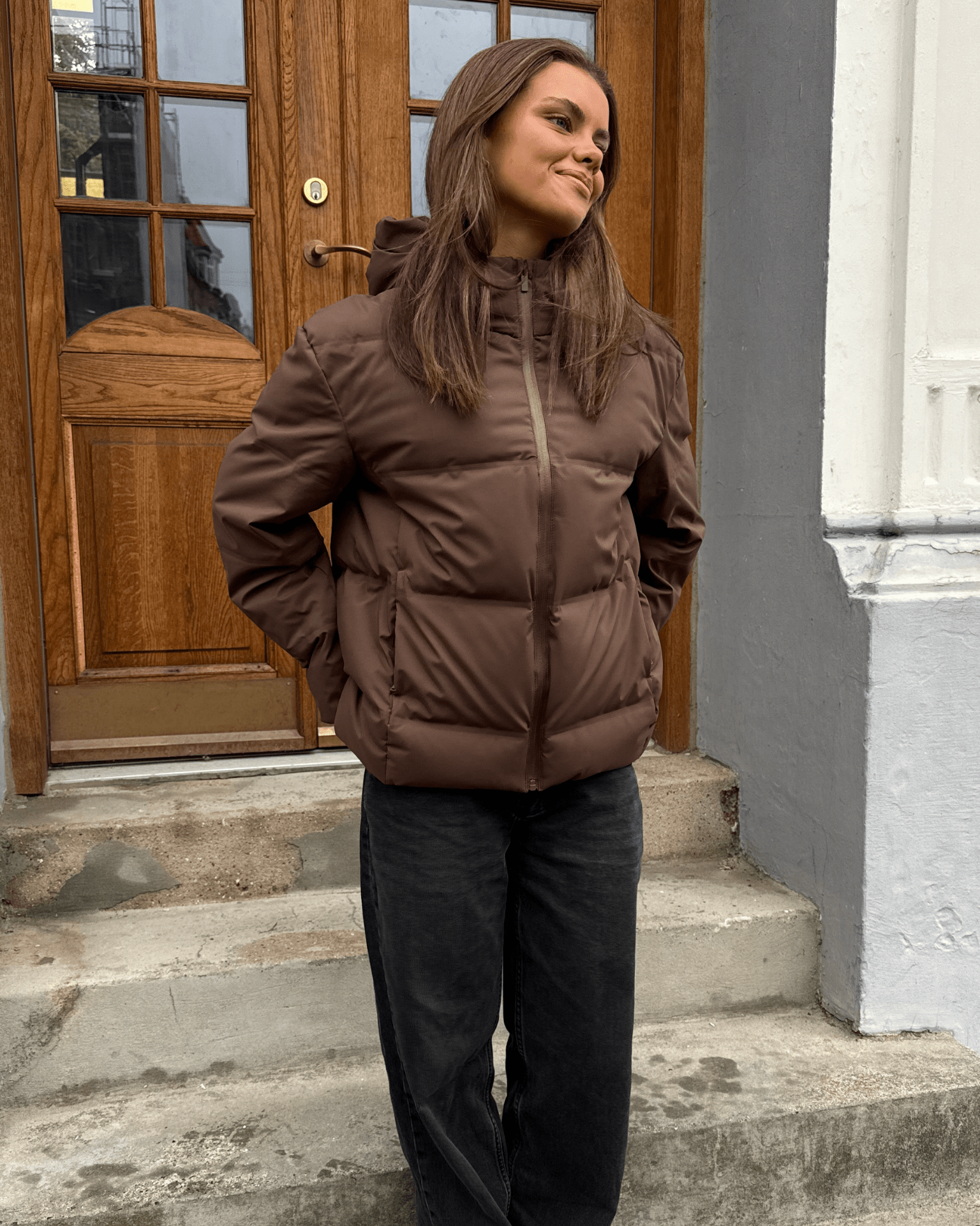 Brun Isa dunjakke i puffer-stil med hætte og lynlås, båret af model på en trappe