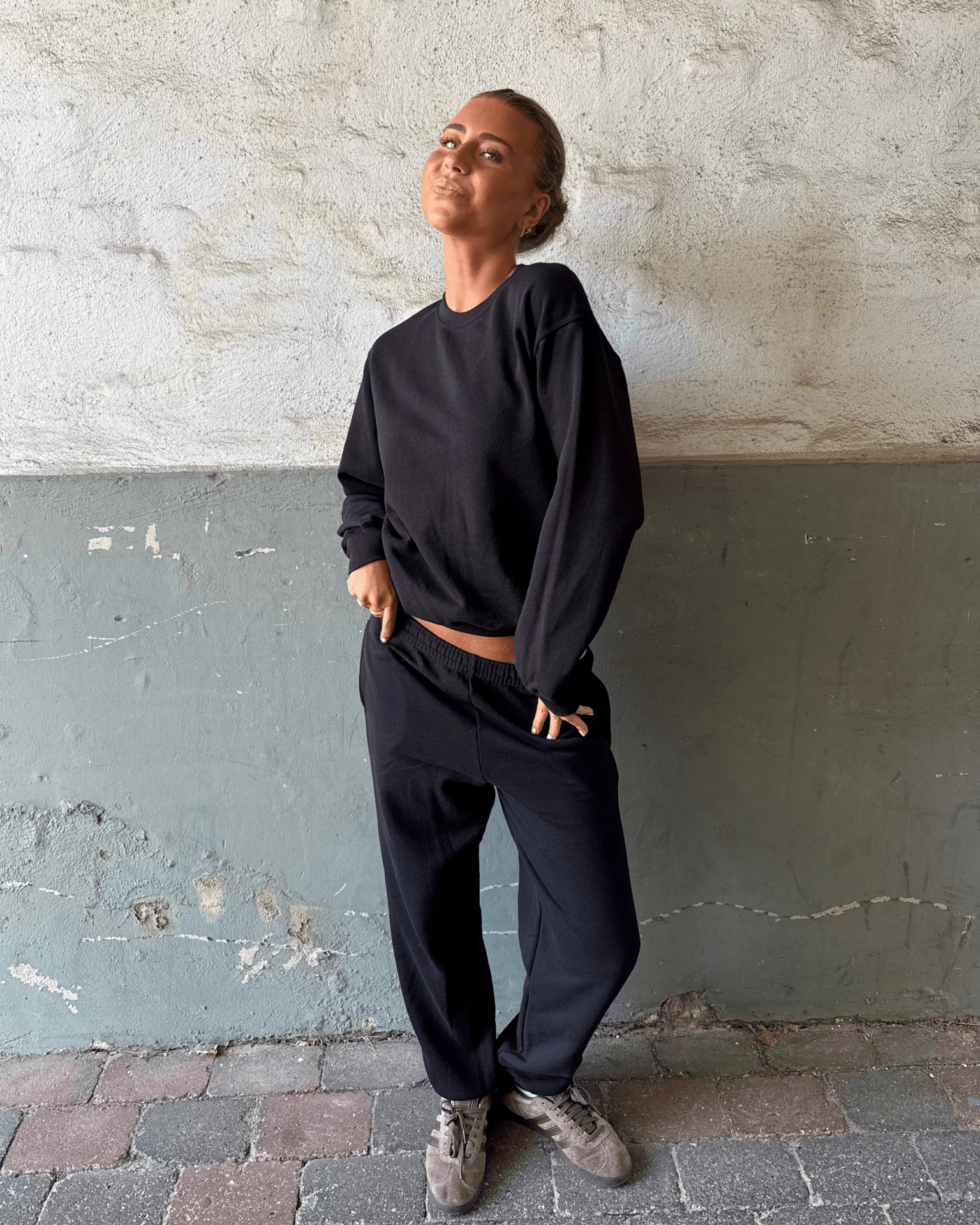 Kvinde i sort Fruit sweatshirt og matchende joggingbukser mod en rå væg