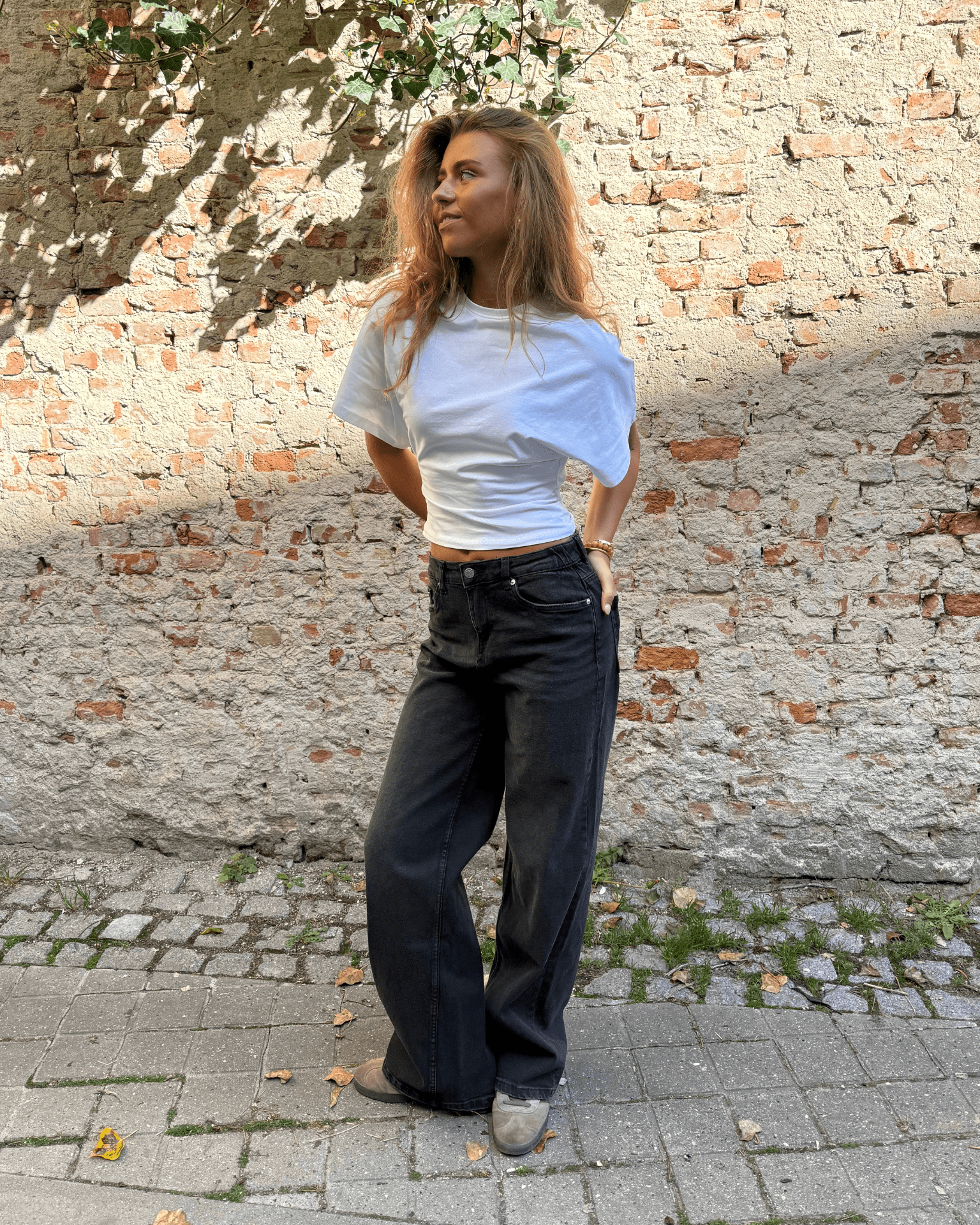 Mørkegrå baggy Alma jeans med mid waist og hvid t-shirt foran en murstensvæg
