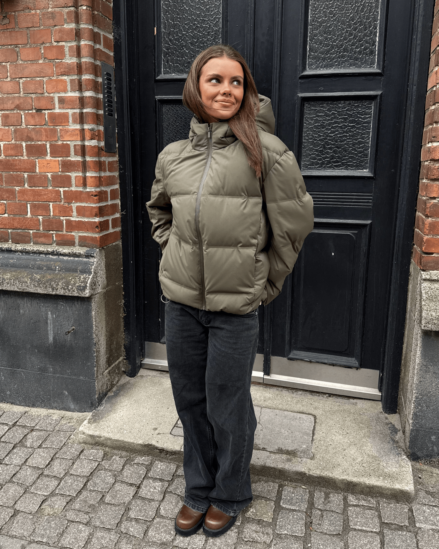 Kvinde i armygrøn Isa dunjakke med hætte og sorte jeans